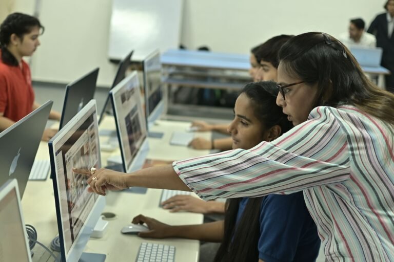 Students and teacher collaborating in a computer lab, discussing digital content.