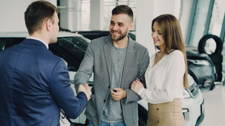 Happy couple finalizing car purchase with salesman in dealership showroom. Bright and welcoming environment.