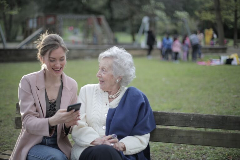 Adult and senior woman sharing a moment on a bench in a sunny park.