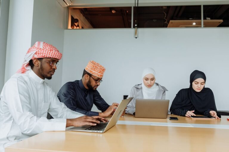 A multicultural team in traditional attire working on laptops in a contemporary office setting.
