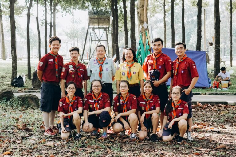 A diverse group of scouts in uniform smiling and posing together in a outdoor camp setting.