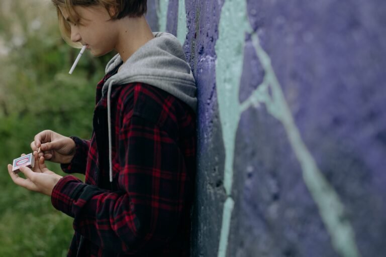Teenager smoking a cigarette against a graffiti wall, representing rebellion.