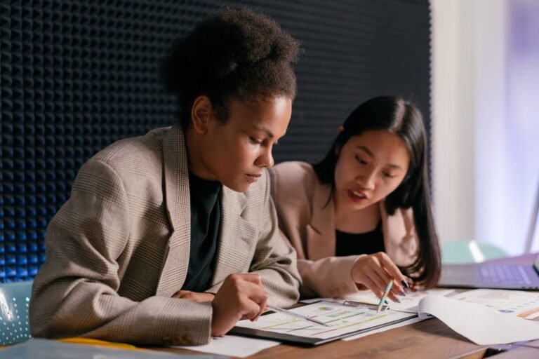 Two businesswomen discussing financial reports in a modern office setting.