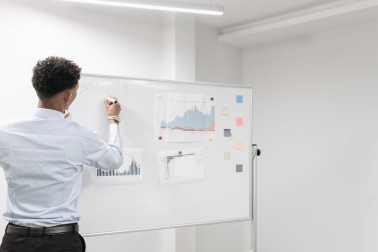 Man reviews COVID-19 data charts on whiteboard in office setting.