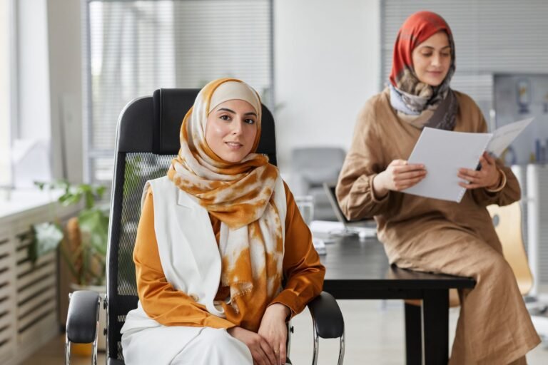 Two businesswomen in hijabs working together in a modern office setting.
