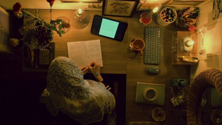 Overhead view of a woman writing in a notebook surrounded by candles, flowers, and a tablet.