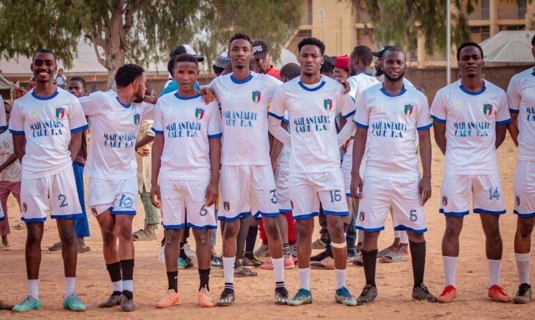Group of young male soccer players in uniforms standing on a field during daytime.