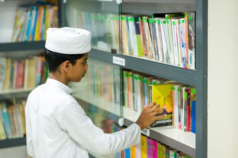 A child in traditional attire picks a book from a well-organized library shelf.