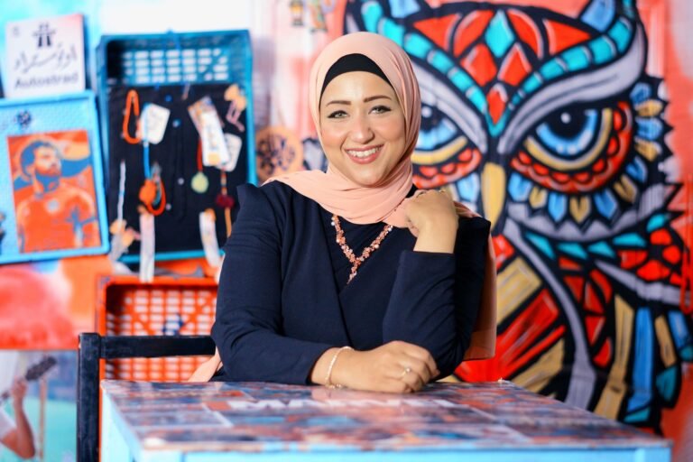 Cheerful woman in hijab posing indoors with a colorful graffiti owl artwork behind her.