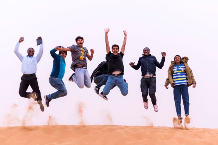 Dynamic photo of six friends jumping in the sand, showing joy and unity outdoors.
