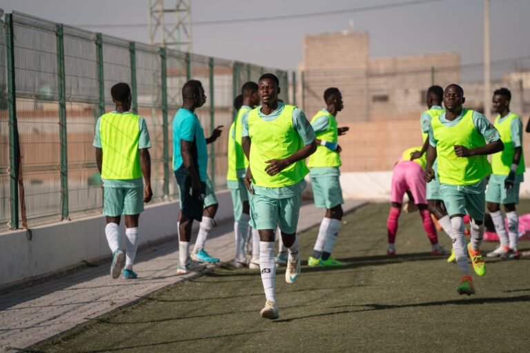 Young male soccer players warming up on a sunny outdoor field, wearing neon green bibs.