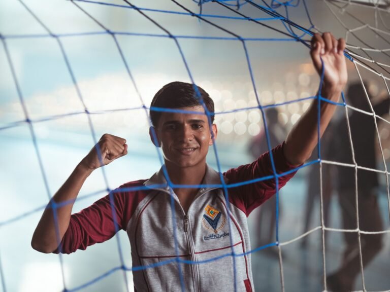 Young male celebrating inside a soccer net, showcasing sports enthusiasm in an indoor setting.